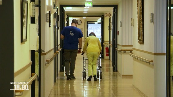 A nurse and a woman with a walker in a hallway of a nursing home.  © Screenshot 