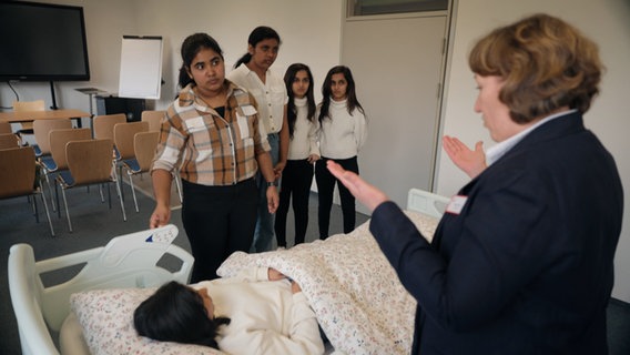 A trainer explains work steps to a group of women at a hospital bed.  © NDR 