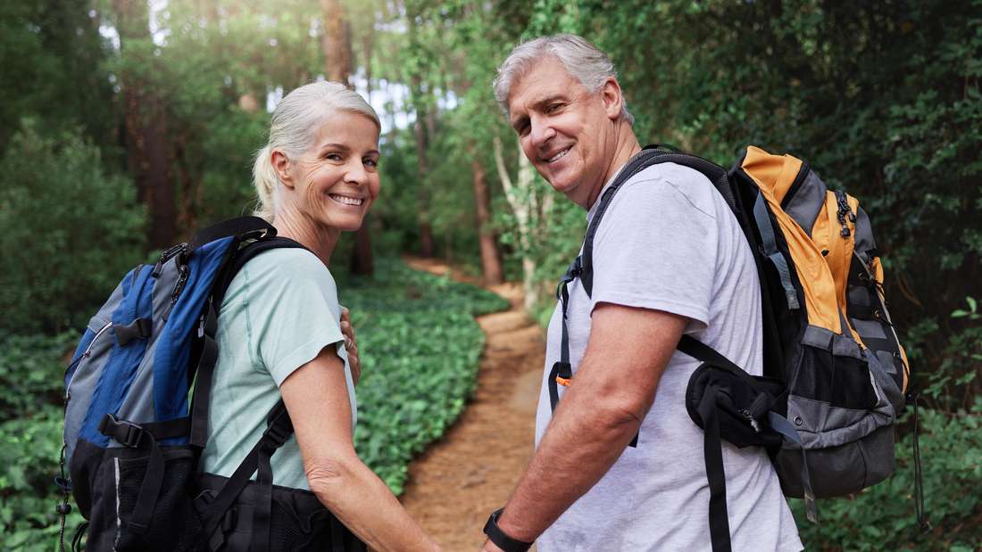 An elderly couple holding hands while hiking.