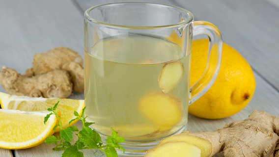 A glass of ginger tea stands on a wooden table, with fresh ginger and a lemon next to it.  © Fotolia.com Photo: juefraphoto